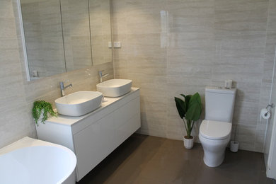 This is an example of a mid-sized contemporary wet room bathroom in Melbourne with white cabinets, a drop-in tub, a one-piece toilet, ceramic tile, cement tiles, a wall-mount sink, solid surface benchtops, brown floor and an open shower.