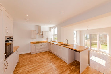 Photo of a small modern l-shaped eat-in kitchen in Sussex with an undermount sink, recessed-panel cabinets, white cabinets, wood benchtops, timber splashback, panelled appliances, light hardwood floors and no island.