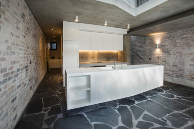 Photo of a large contemporary galley eat-in kitchen in Sydney with an undermount sink, flat-panel cabinets, white cabinets, solid surface benchtops, grey splashback, stone slab splashback, black appliances, cement tiles, with island and grey floor.