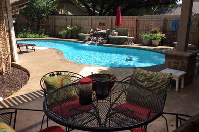 This is an example of a mid-sized country backyard kidney-shaped natural pool in Dallas with stamped concrete and a water feature.