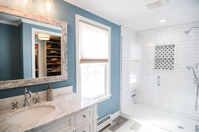 This is an example of a large transitional master bathroom in Boston with recessed-panel cabinets, white cabinets, an alcove shower, a two-piece toilet, white tile, subway tile, blue walls, ceramic floors, an undermount sink, marble benchtops, beige floor, a hinged shower door and white benchtops.