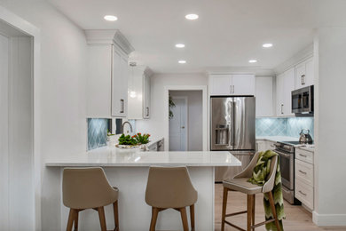Foto på ett mellanstort funkis vit kök, med en undermonterad diskho, skåp i shakerstil, vita skåp, bänkskiva i kvarts, blått stänkskydd, stänkskydd i keramik, rostfria vitvaror, vinylgolv, en halv köksö och brunt golv