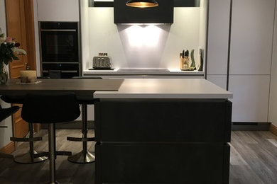 This is an example of a contemporary eat-in kitchen in Other with white cabinets, laminate benchtops, white splashback, with island and white benchtop.