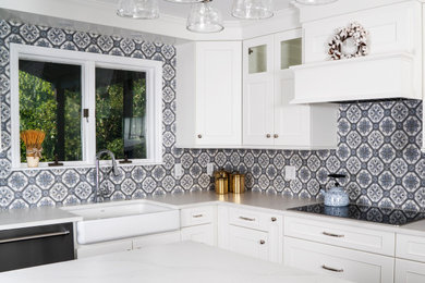 Eat-in kitchen - mid-sized transitional l-shaped medium tone wood floor and brown floor eat-in kitchen idea in St Louis with a farmhouse sink, recessed-panel cabinets, white cabinets, quartz countertops, blue backsplash, ceramic backsplash, stainless steel appliances, an island and white countertops