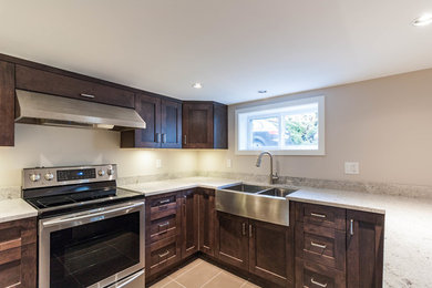 Eat-in kitchen - mid-sized transitional u-shaped ceramic tile and beige floor eat-in kitchen idea in Vancouver with a farmhouse sink, shaker cabinets, dark wood cabinets, granite countertops, stainless steel appliances and a peninsula