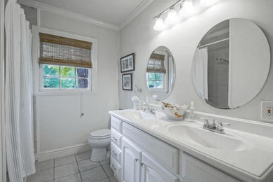 Example of a large classic 3/4 porcelain tile and gray floor bathroom design in New Orleans with raised-panel cabinets, white cabinets, a two-piece toilet, white walls, an integrated sink and quartz countertops