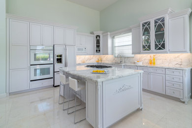 Photo of a large traditional l-shaped open plan kitchen in Miami with an undermount sink, recessed-panel cabinets, white cabinets, marble benchtops, multi-coloured splashback, stone slab splashback, stainless steel appliances, porcelain floors and with island.