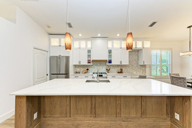Mid-sized trendy single-wall porcelain tile, beige floor and vaulted ceiling eat-in kitchen photo in Tampa with a drop-in sink, shaker cabinets, white cabinets, quartzite countertops, beige backsplash, stone tile backsplash, stainless steel appliances, an island and white countertops