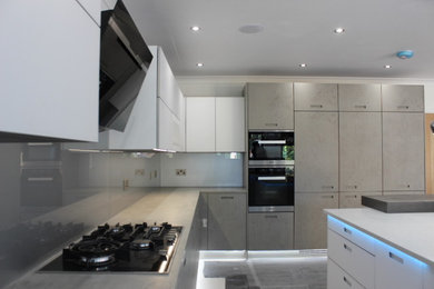 Inredning av ett modernt stort grå grått kök, med en integrerad diskho, bruna skåp, bänkskiva i koppar, grått stänkskydd, stänkskydd i glaskakel, svarta vitvaror, klinkergolv i keramik, en köksö och beiget golv