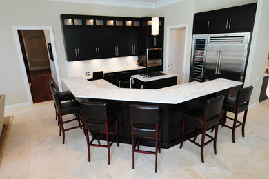 Mid-sized transitional l-shaped open plan kitchen in Tampa with multiple islands, an undermount sink, flat-panel cabinets, black cabinets, marble benchtops, white splashback, stone slab splashback, stainless steel appliances, porcelain floors, beige floor and grey benchtop.