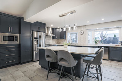 Example of a mid-sized transitional l-shaped ceramic tile and gray floor eat-in kitchen design in Edmonton with an undermount sink, shaker cabinets, gray cabinets, quartz countertops, white backsplash, ceramic backsplash, stainless steel appliances, an island and white countertops