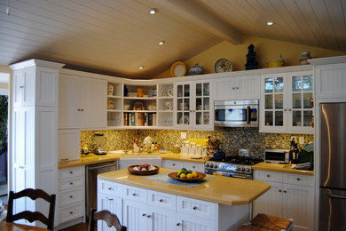 Inspiration for a large traditional l-shaped eat-in kitchen in Orange County with a farmhouse sink, shaker cabinets, white cabinets, solid surface benchtops, multi-coloured splashback, mosaic tile splashback, stainless steel appliances, with island and dark hardwood floors.