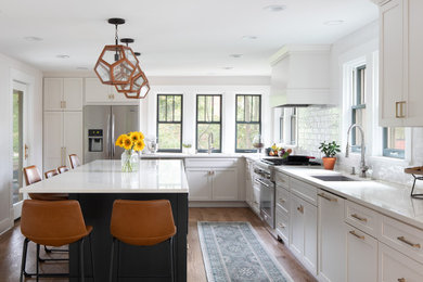 Example of a transitional l-shaped medium tone wood floor and brown floor eat-in kitchen design in Other with a drop-in sink, shaker cabinets, white cabinets, quartzite countertops, white backsplash, subway tile backsplash, stainless steel appliances, an island and white countertops