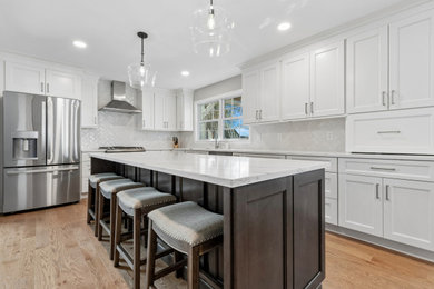 Inspiration for a mid-sized transitional l-shaped light wood floor and brown floor kitchen remodel in Philadelphia with an undermount sink, shaker cabinets, white cabinets, quartz countertops, white backsplash, porcelain backsplash, stainless steel appliances, an island and white countertops