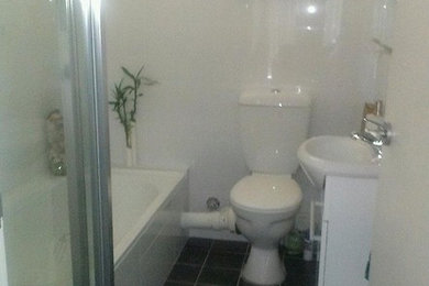 Inredning av ett litet en-suite badrum, med vita skåp, en toalettstol med separat cisternkåpa, vit kakel, keramikplattor, vita väggar, klinkergolv i keramik, laminatbänkskiva och grått golv