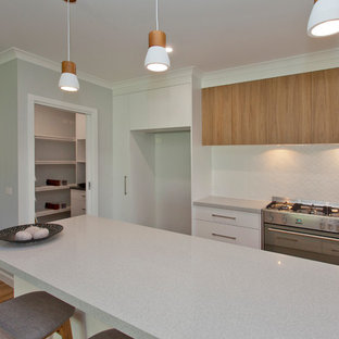 Bild på ett stort funkis grå grått kök, med en nedsänkt diskho, släta luckor, skåp i ljust trä, bänkskiva i kvarts, vitt stänkskydd, stänkskydd i keramik, rostfria vitvaror, linoleumgolv, en köksö och brunt golv