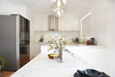Large contemporary u-shaped eat-in kitchen in Melbourne with a single-bowl sink, flat-panel cabinets, white cabinets, quartz benchtops, white splashback, ceramic splashback, stainless steel appliances, laminate floors, with island, brown floor and white benchtop.