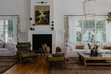 Cette photo montre un très grand salon tendance avec un mur blanc, un sol en bois brun, une cheminée standard, un manteau de cheminée en plâtre, un sol marron et un plafond voûté.