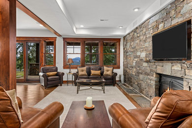 Example of a large mountain style open concept dark wood floor, brown floor, coffered ceiling and wood wall living room design with white walls, a standard fireplace, a stone fireplace and a wall-mounted tv