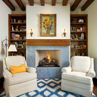 Bild på ett medelhavsstil hemmabibliotek, med vita väggar, mellanmörkt trägolv, en standard öppen spis, en spiselkrans i trä och ett fristående skrivbord