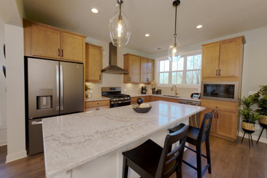Example of a large farmhouse l-shaped medium tone wood floor and brown floor open concept kitchen design in Louisville with an undermount sink, recessed-panel cabinets, medium tone wood cabinets, quartzite countertops, white backsplash, ceramic backsplash, stainless steel appliances, an island and gray countertops
