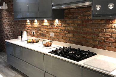 Photo of an urban galley open plan kitchen in Manchester with a submerged sink, flat-panel cabinets, grey cabinets, quartz worktops, black appliances, an island and white worktops.