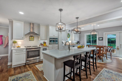 Large minimalist single-wall medium tone wood floor, brown floor and tray ceiling eat-in kitchen photo in Richmond with flat-panel cabinets, white cabinets, granite countertops, white backsplash, ceramic backsplash, stainless steel appliances, an island, white countertops and a farmhouse sink