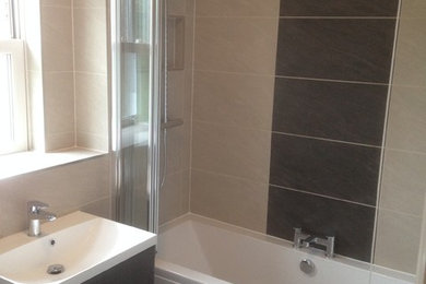 Inspiration for a contemporary bathroom in Buckinghamshire with flat-panel cabinets, brown cabinets, a built-in bath, a shower/bath combination, beige tiles, porcelain tiles, multi-coloured walls, porcelain flooring and a wall-mounted sink.