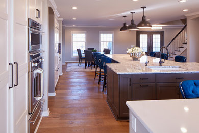 Eat-in kitchen - large transitional u-shaped medium tone wood floor and brown floor eat-in kitchen idea in Omaha with a drop-in sink, shaker cabinets, white cabinets, quartz countertops, gray backsplash, glass tile backsplash, stainless steel appliances and an island