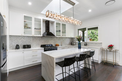 Inspiration for a mid-sized modern l-shaped kitchen pantry in Melbourne with a farmhouse sink, shaker cabinets, white cabinets, quartz benchtops, grey splashback, porcelain splashback, black appliances, dark hardwood floors, with island, brown floor and white benchtop.