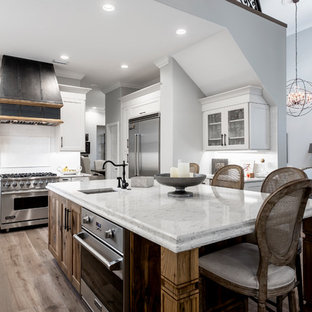 This is an example of a large traditional u-shaped kitchen pantry in Tampa with a farmhouse sink, shaker cabinets, quartz benchtops, white splashback, porcelain splashback, stainless steel appliances, medium hardwood floors, with island, brown floor, white benchtop and white cabinets.
