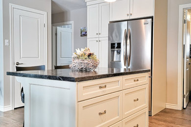 Inspiration for a mid-sized timeless single-wall medium tone wood floor and brown floor eat-in kitchen remodel in Other with a double-bowl sink, shaker cabinets, white cabinets, granite countertops, beige backsplash, stone tile backsplash, stainless steel appliances, an island and black countertops