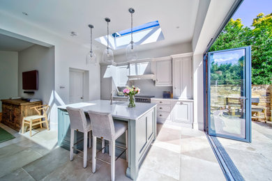 This is an example of a contemporary grey and teal kitchen in London with a submerged sink, shaker cabinets, white cabinets, quartz worktops, white splashback, engineered quartz splashback, black appliances, limestone flooring, an island, beige floors, white worktops and feature lighting.
