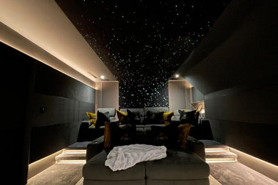 Photo of a medium sized contemporary home cinema in Hertfordshire with black walls, carpet, a projector screen, beige floors and feature lighting.