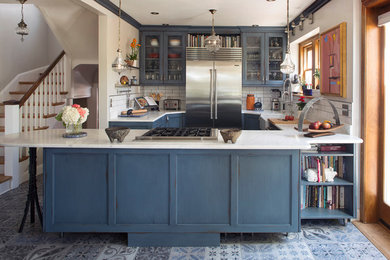 Inspiration for a mid-sized transitional open plan kitchen in Denver with a farmhouse sink, glass-front cabinets, blue cabinets, marble benchtops, white splashback, ceramic splashback, stainless steel appliances, ceramic floors, blue floor and white benchtop.