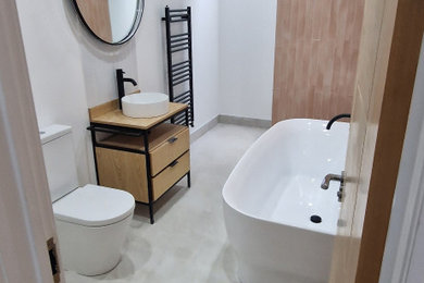Inspiration for a medium sized grey and pink ensuite bathroom in London with light wood cabinets, a freestanding bath, pink tiles, white walls, a vessel sink, wooden worktops, grey floors, brown worktops, feature lighting, a single sink and a freestanding vanity unit.