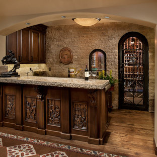 フェニックスの中サイズの地中海スタイルのおしゃれなウェットバー (濃色木目調キャビネット、レイズドパネル扉のキャビネット、コンクリートカウンター、ベージュキッチンパネル、濃色無垢フローリング、茶色い床、石タイルのキッチンパネル) の写真