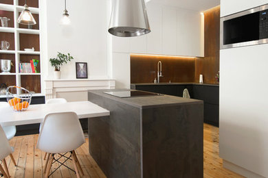 Large contemporary open plan kitchen in Toulouse with an undermount sink, black cabinets, marble benchtops, metallic splashback, black appliances, light hardwood floors, with island and black benchtop.