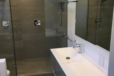 Inspiration for a contemporary master beige tile and porcelain tile ceramic tile alcove shower remodel in Milwaukee with flat-panel cabinets, gray cabinets, white walls, an integrated sink and solid surface countertops