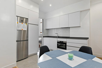 Imagen de cocinas en L tradicional renovada pequeña abierta sin isla con fregadero bajoencimera, armarios con paneles lisos, puertas de armario blancas, salpicadero metalizado, salpicadero de azulejos de cerámica, electrodomésticos de acero inoxidable, suelo de baldosas de cerámica, suelo gris y encimeras negras