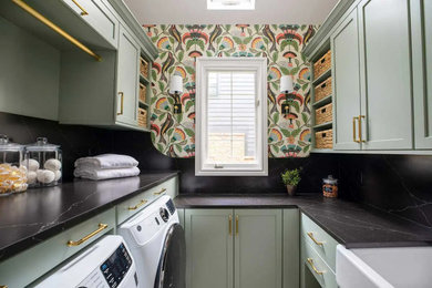 Example of a mid-sized transitional u-shaped porcelain tile, beige floor and wallpaper utility room design in Detroit with a farmhouse sink, shaker cabinets, green cabinets, quartz countertops, black backsplash, quartz backsplash, multicolored walls, a side-by-side washer/dryer and black countertops