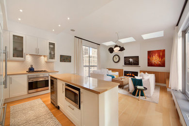 Open concept kitchen - mid-sized contemporary l-shaped light wood floor and beige floor open concept kitchen idea in New York with shaker cabinets, white cabinets, solid surface countertops, white backsplash, brick backsplash, stainless steel appliances, an island and an undermount sink