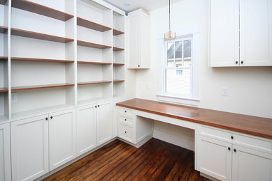 Transitional built-in desk dark wood floor study room photo in Raleigh with white walls