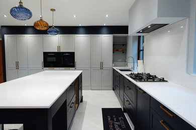 Large classic single-wall open plan kitchen in Other with a built-in sink, shaker cabinets, medium wood cabinets, quartz worktops, white splashback, engineered quartz splashback, black appliances, porcelain flooring, an island, white floors, white worktops, a coffered ceiling and feature lighting.