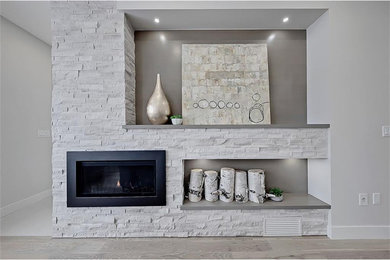 Example of a mid-sized minimalist open concept medium tone wood floor and gray floor living room design in Calgary with a bar, white walls, a standard fireplace, a stone fireplace and a media wall