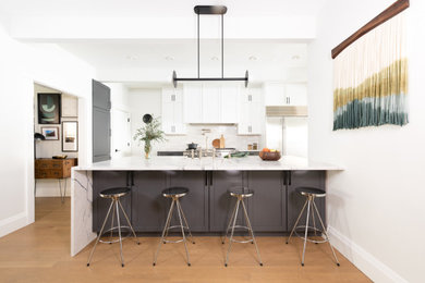 Large transitional single-wall light wood floor and brown floor eat-in kitchen photo in Chicago with a drop-in sink, flat-panel cabinets, white cabinets, quartz countertops, white backsplash, ceramic backsplash, stainless steel appliances, an island and white countertops