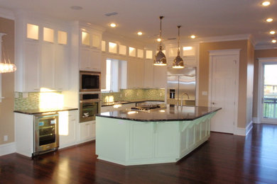 Open concept kitchen - large transitional l-shaped dark wood floor and brown floor open concept kitchen idea in Austin with a double-bowl sink, shaker cabinets, white cabinets, quartzite countertops, green backsplash, mosaic tile backsplash, stainless steel appliances, an island and black countertops