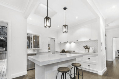 Inspiration for a small traditional galley open plan kitchen in Melbourne with an undermount sink, shaker cabinets, white cabinets, quartz benchtops, white splashback, subway tile splashback, stainless steel appliances, medium hardwood floors, with island, brown floor and grey benchtop.