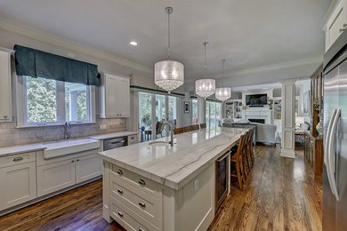 Example of a large classic u-shaped dark wood floor and brown floor eat-in kitchen design in Charlotte with a farmhouse sink, shaker cabinets, white cabinets, gray backsplash, subway tile backsplash, stainless steel appliances, an island and white countertops