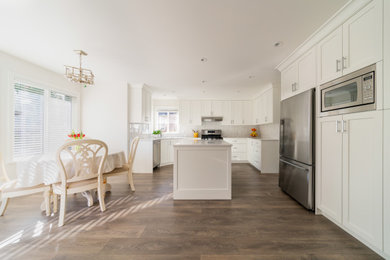 Example of a large classic u-shaped medium tone wood floor and brown floor eat-in kitchen design in Vancouver with shaker cabinets, white cabinets, quartz countertops, gray backsplash, mosaic tile backsplash, stainless steel appliances, an island and white countertops